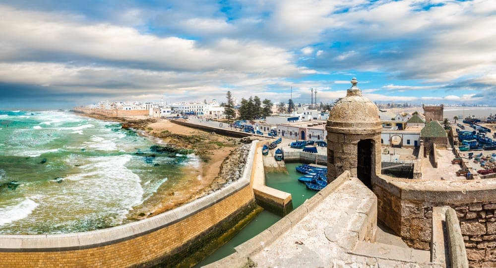 Aerial view of Essaouira's harbor with rows of blue fishing boats beside the stone watchtower