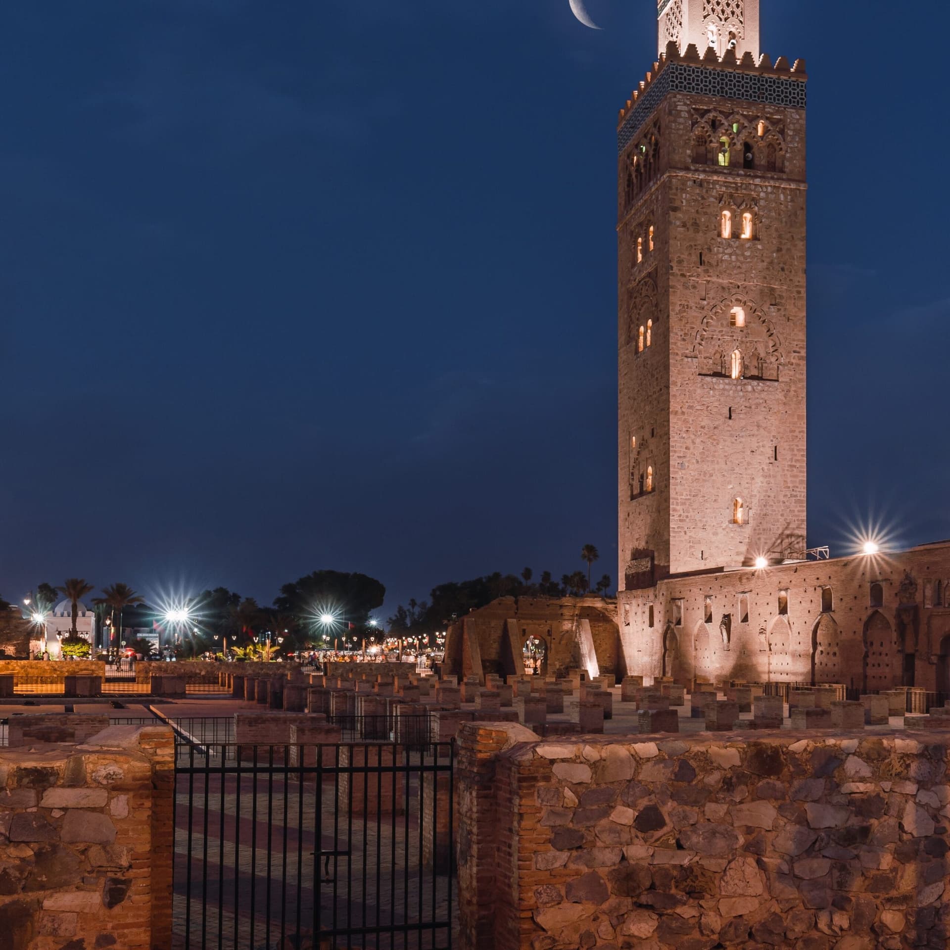 Koutoubia Mosque illuminated at night under a crescent moon in Marrakech