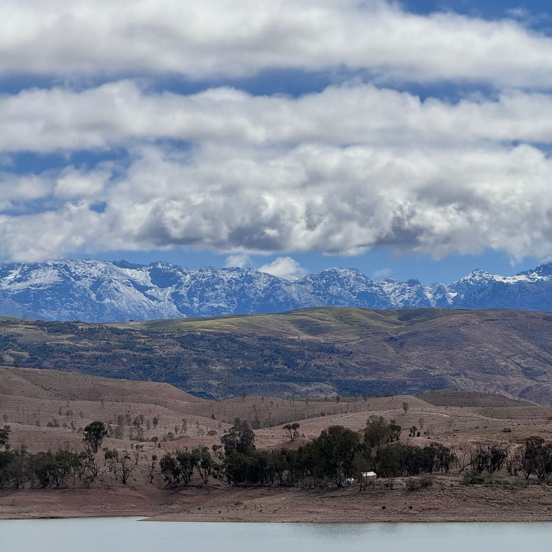 Reservoir lake with rolling hills and the snow-capped Atlas Mountains in the background